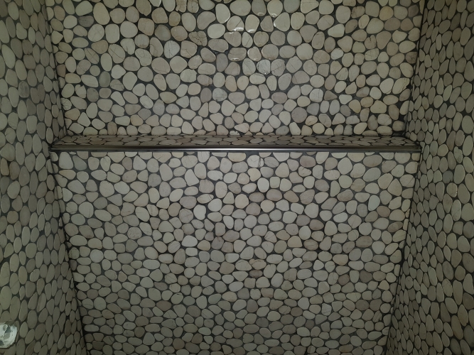 Flisearbejde med naturstensmosaik og integreret hylde i Spøttrup